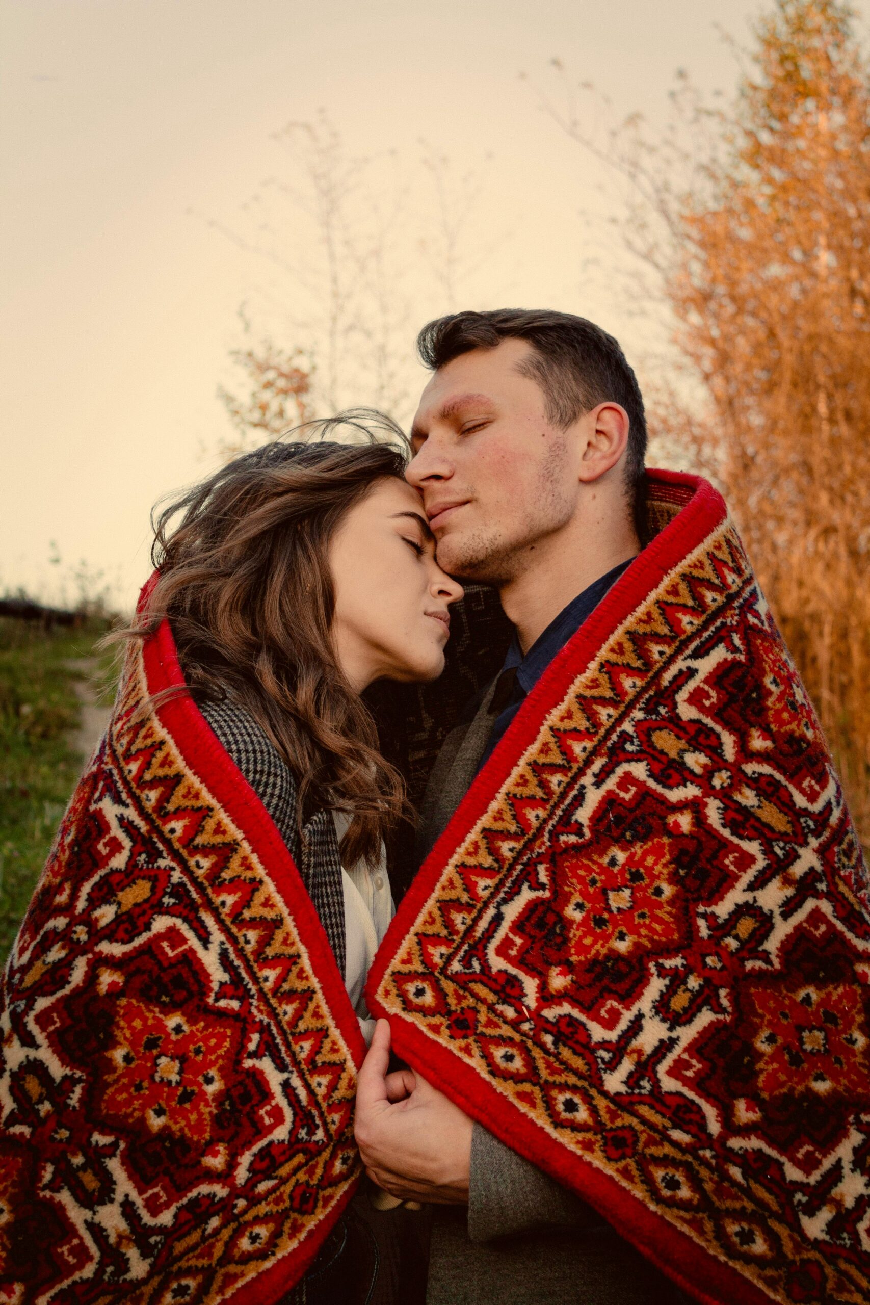A loving couple embraces outdoors, wrapped in a colorful blanket during fall in Lviv, Ukraine.