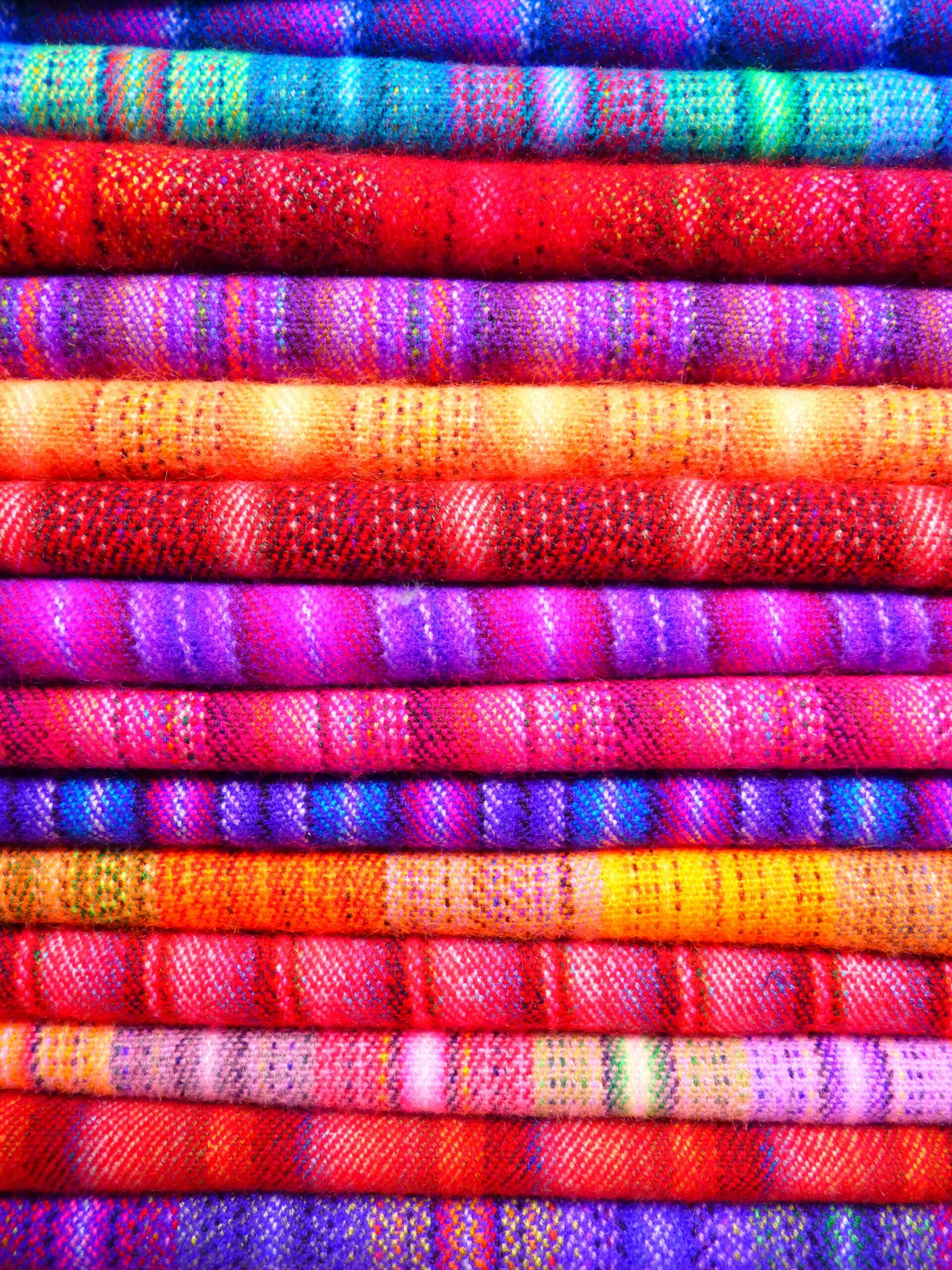 Close-up of vibrant and colorful textiles stacked in layers, showcasing intricate patterns and designs.